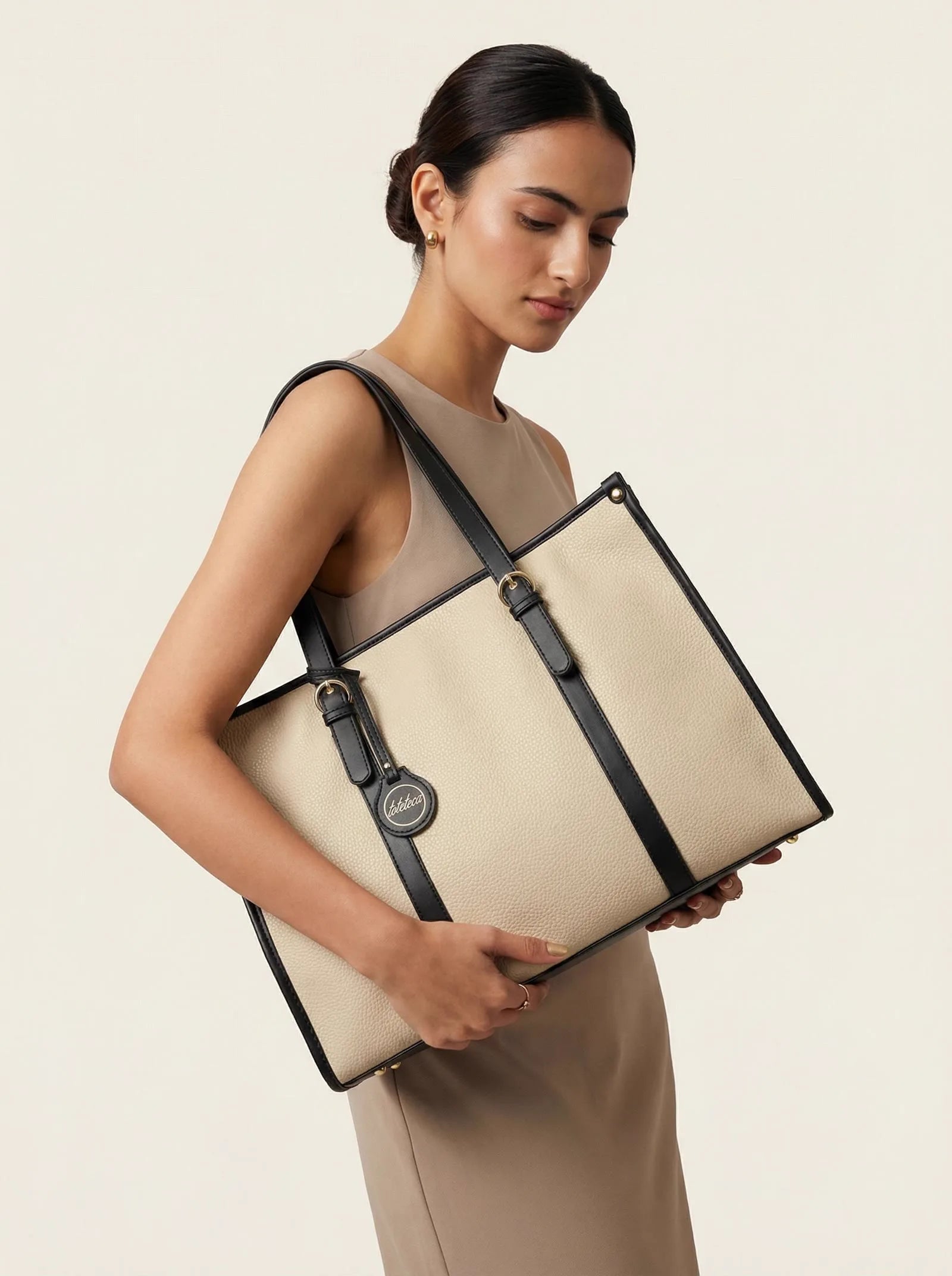 Ivory Toteteca tote with black straps carried by a model in a taupe dress