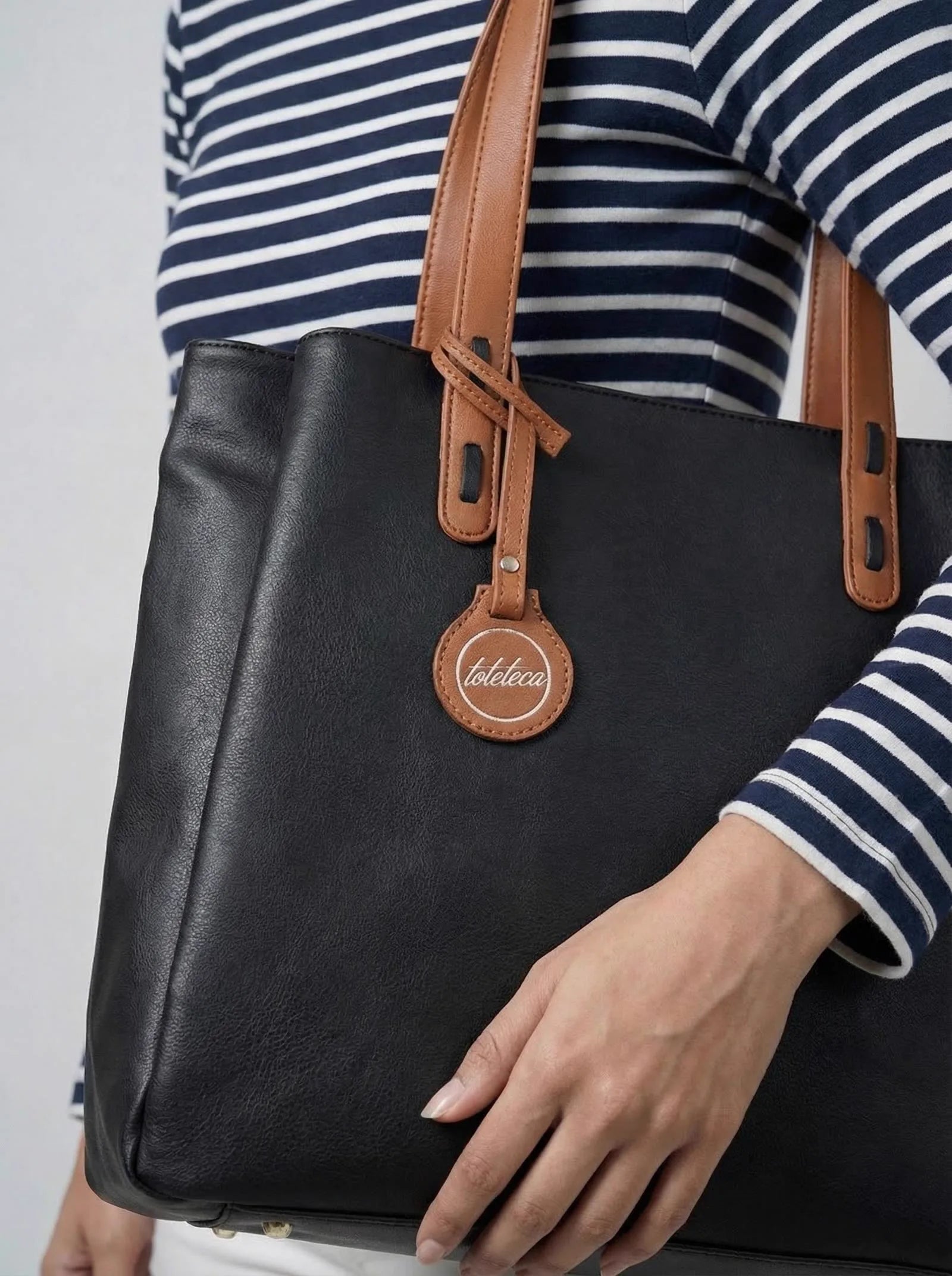 Close-up of a black Toteteca tote with tan handles and the round toteteca logo charm