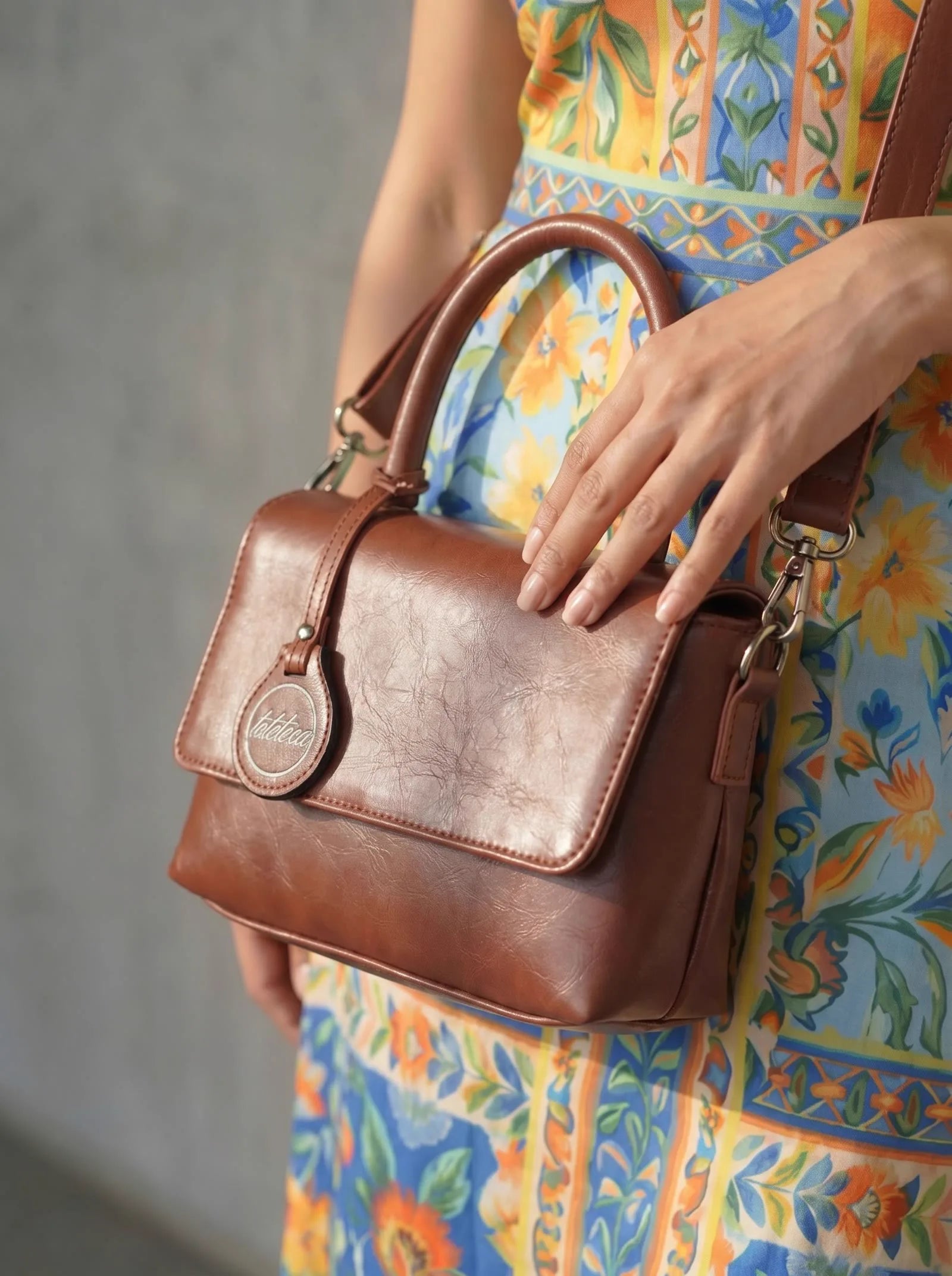 Tan Toteteca top-handle satchel with logo charm, styled with a floral summer dress