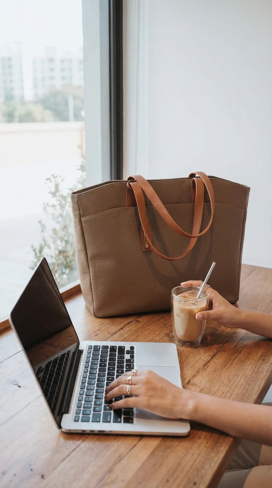 Tan Toteteca tote on a cafe table beside a laptop and iced coffee