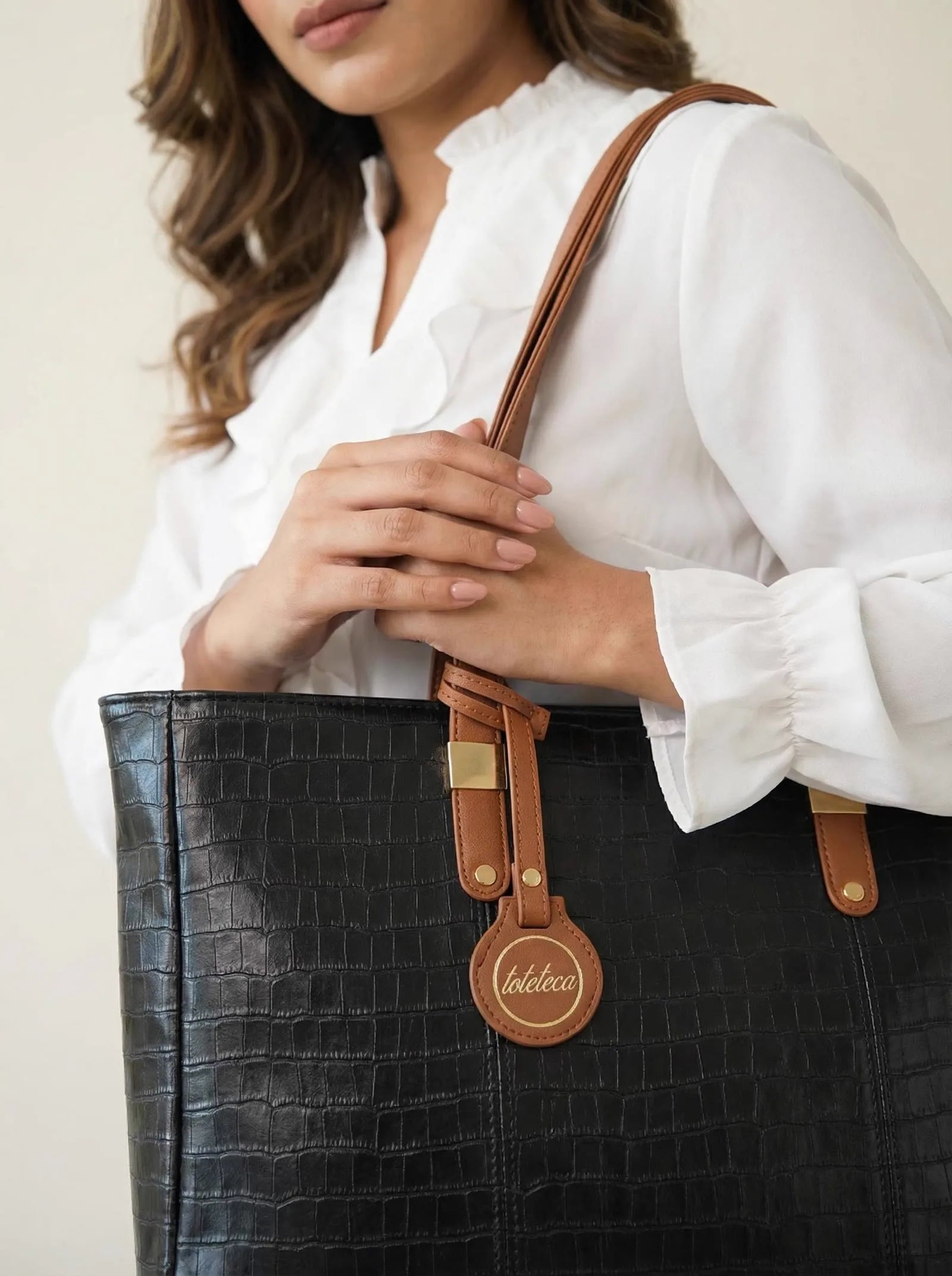 The round toteteca logo charm in tan leather on a black croc-texture tote