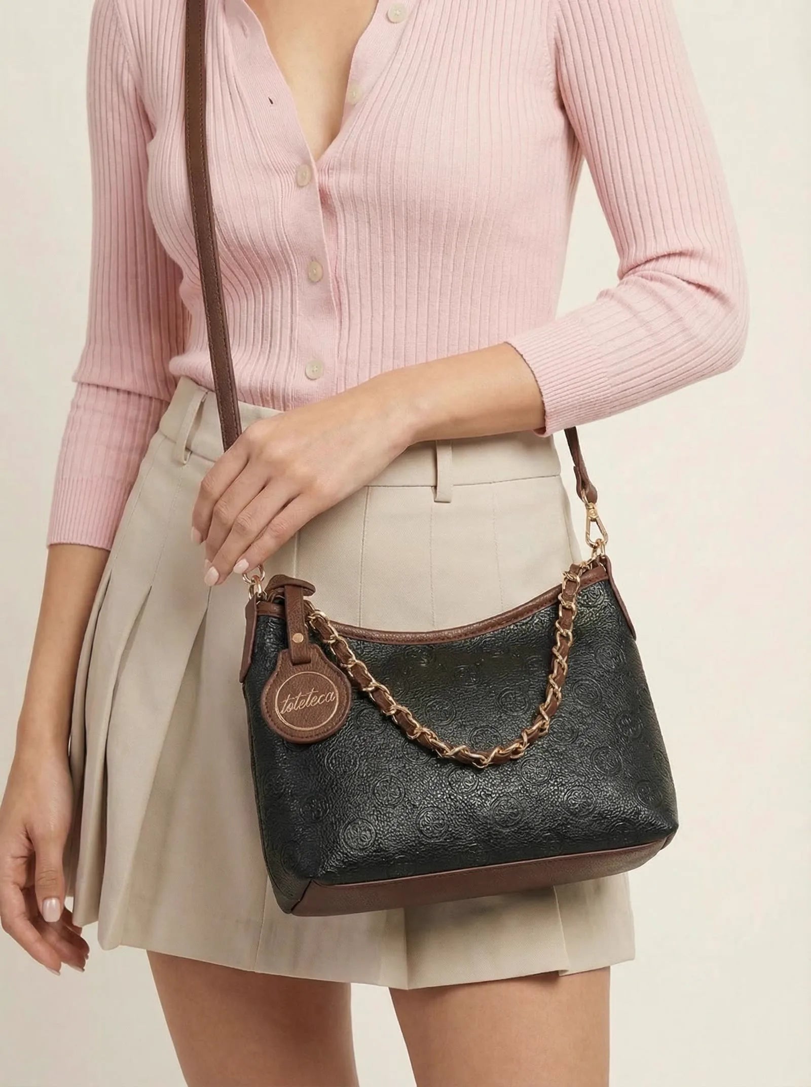 Black monogram-embossed Toteteca hobo bag with gold chain, worn with a pink cardigan