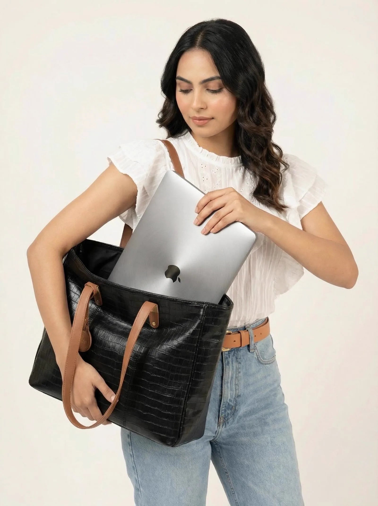 Woman sliding a laptop into a black croc-texture Toteteca office tote with tan handles