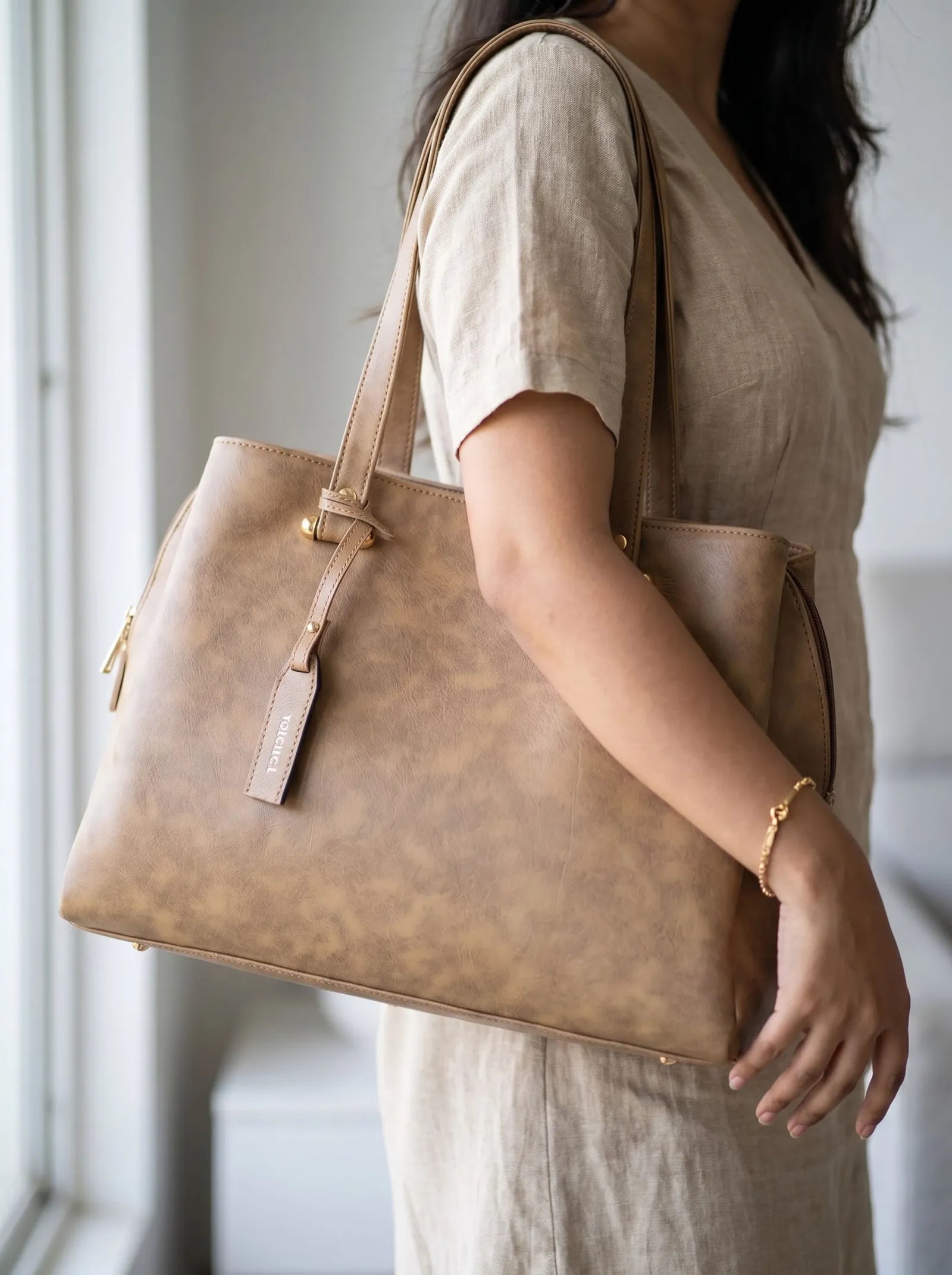 Camel Toteteca office tote on the shoulder of a woman in a linen dress