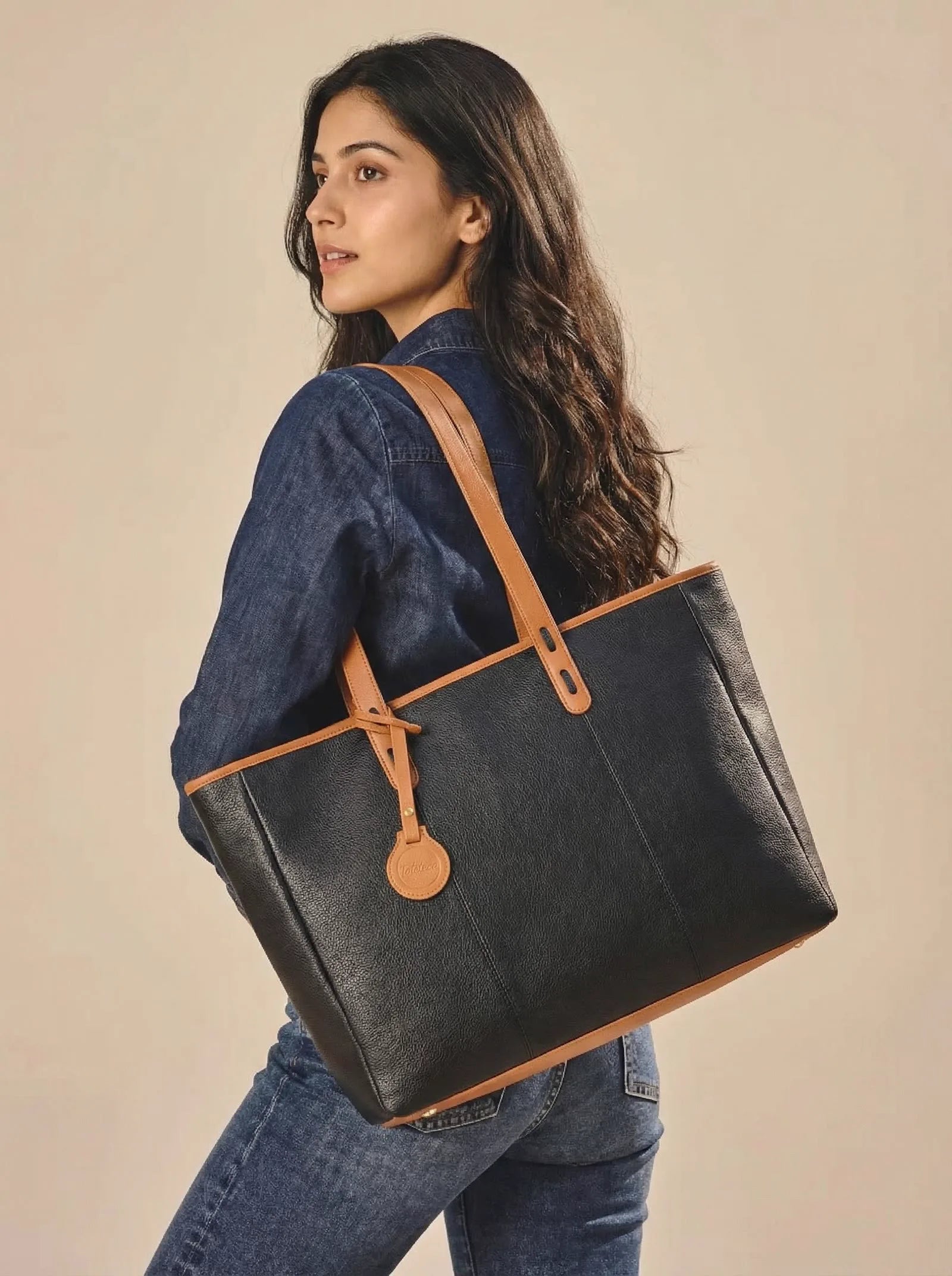 Model in a denim shirt carrying a black Toteteca tote with tan straps