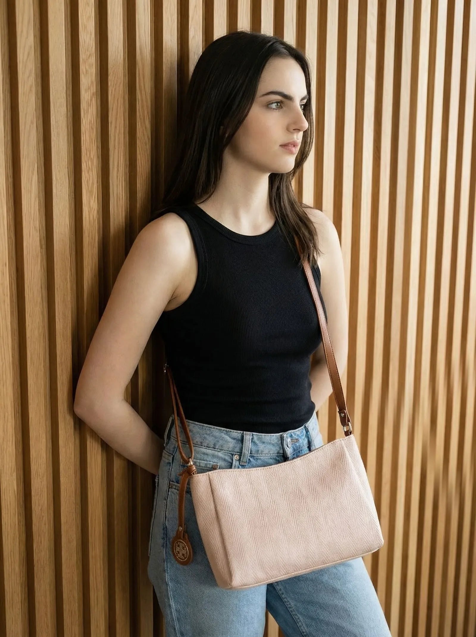 Model in black with a blush pink Toteteca crossbody against a wood-slat wall