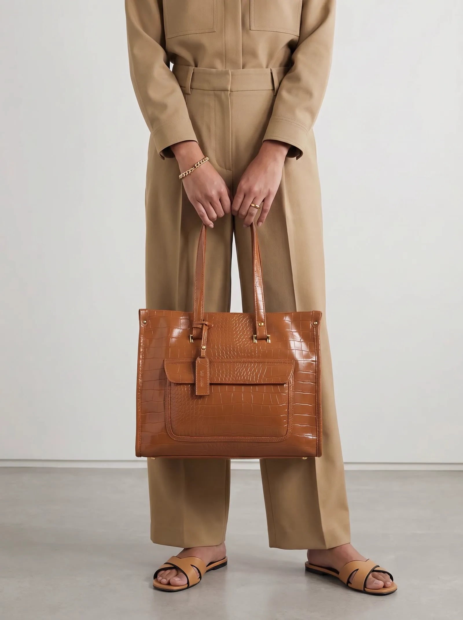 Model in a beige suit holding a tan croc-texture Toteteca tote in golden light