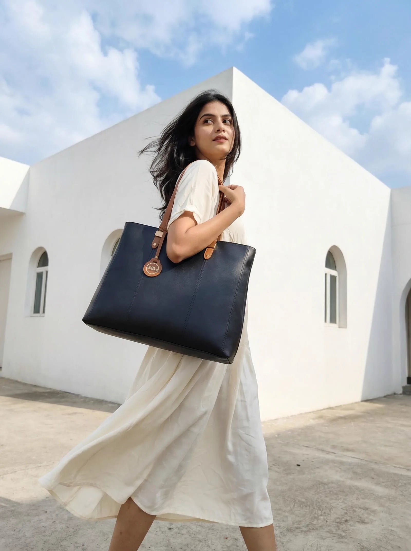 Navy Toteteca tote with tan straps carried against a white building and blue sky