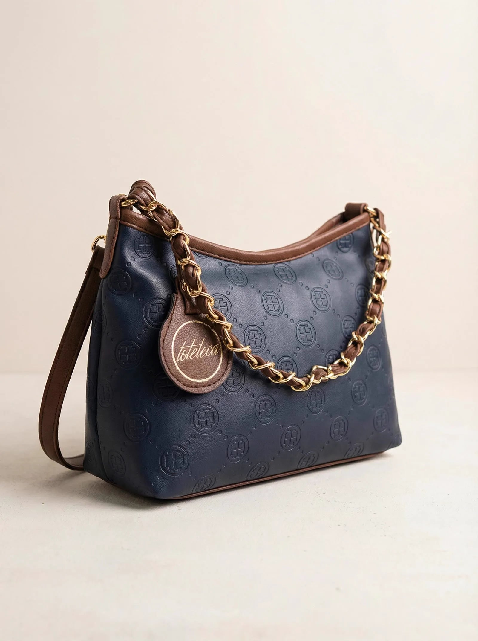 Navy monogram-embossed Toteteca hobo bag with braided gold chain — studio product shot